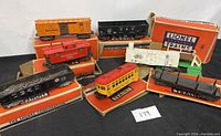 Seven vintage Lionel train cars displayed with their original boxes, including Baby Ruth, Pennsylvania, and other freight cars.