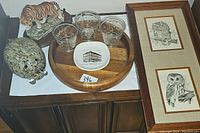 Photo showing the assortment of animal figurines including a tiger and pig, three Fred Press glasses, a wooden tray with small ceramic plate, and a framed ovwl art print.