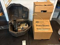 Craftsman chainsaw inside a black plastic carrying case beside Craftsman electric power blower in original labeled cardboard box.
