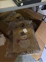 Box of stacked brown paper shopping bags featuring a snowman design, handles visible.