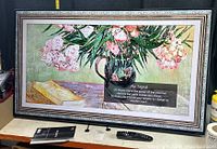 Front view of LG NanoCell TV powered on displaying art, with remote and manual on table