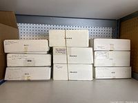 Eight white boxes of Norman Rockwell Christmas Legacy Collection plates stacked on shelf, some labeled 'FRAGILE'.