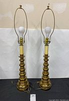 Pair of heavy brass table lamps side by side showing full height and base design.