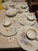 Photo showing 5 snack plates with floral designs paired with matching cups arranged on a table.