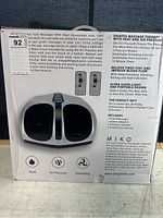 Miko Shiatsu Foot Massager box front showing foot openings and basic features: heat, air pressure, kneading. Product image and dual wireless remote illustration.