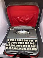 Front view of Smith-Corona Skyriter typewriter inside open black carrying case with red interior lining.