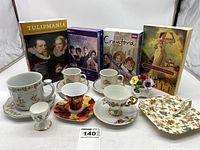 Wide view showing all tea cups with saucers, three movie collections on DVD, two books, and small flower vase arranged on a white background