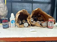 Vintage cans arranged on table including Pepsi can, pump dispenser can, and multiple cans in brown paper bags, one with a sports-themed promotional print.