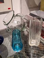 Photo showing three mid century glass items: clear fish pitcher, textured clear vase, small blue vase.