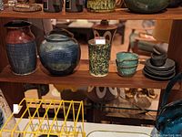 Photo showing five mid century ceramic items on a wooden shelf including various vases, jar, and cups with saucers