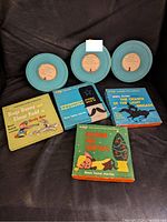 Three blue metal 8mm film reels and four vintage illustrated cardboard boxes with film titles and characters