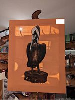 Brown fabric panel with pelican standing on a post, hung on wooden frame or stand indoors.