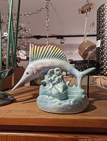 Photo of a ceramic fish figurine with a glossy glaze in pale green and blue hues, detailed fins, and a marine-themed base.