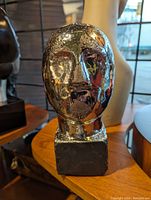 Front view of the chrome head sculpture highlighting surface condition and facial features.