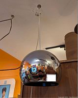 Chrome spherical pendant light hanging from ceiling with reflective surface showing room reflection.