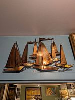 Copper metal art wall sculpture showing multiple stylized sailboats with curved bases, varying sails and mast flags.