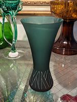Tall green glass vase with a flared top and silver geometric accents near the base.