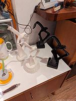 Four ceramic seagulls, two white and two black, displayed on a white surface near other objects, showing their abstract design and mounting bases.