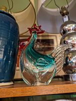 Single glass rooster figurine displayed on shelf between other decorative items.