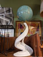 Globe sculpture featuring a blue globe on a white curved abstract base, photographed from the front.