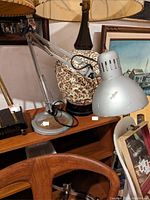 Photo shows a vintage industrial adjustable metal desk lamp with a round base and articulated arm placed on wooden furniture, alongside other decorative objects.