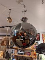 Photo showing a large spherical pendant light fixture with a polished chrome finish and cut-out parts hanging from the ceiling.
