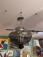 Mid century glass pendant light fixture suspended from ceiling with metal chains and canopy. Shows large smoky-tinted glass globe and inner candle bulb holders.
