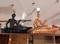 Front view of two chalkware rowing man table lamps, one black finish and one metallic copper finish, showing sculpted figures and lamp hardware.