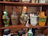 Photo showing set of five mid century ceramic vases on a wooden shelf, varying in shape, color, and design.