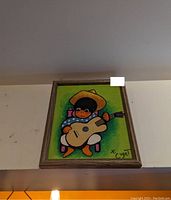 Framed signed original painting showing a boy with a guitar, wearing a yellow hat and blue polka-dot shirt, on green background.