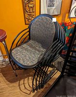 Photo of six stacking chairs with black metal frames and patterned padded seats and backrests.