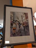 Framed watercolor painting depicting a street scene with pedestrians and urban buildings.