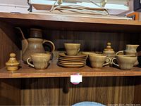 Brown ceramic tea set displayed on a wooden shelf including teapot, cups, bowls, saucers, sugar bowl and creamer.