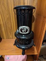 Front view of the black vintage Aladdin heater stove showing perforated ventilation holes, Aladdin badge, rounded top and legs