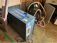 Side view of gray King Canada air cleaner unit with power cord and vent, placed on shed floor.