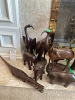 Seven wood carved animal figurines arranged on floor. Includes birds, elephants, rhinoceros, and alligator.