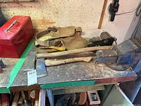 Overview of lot showing axes, toolbox, tool belt, gloves, and vises on workbench.