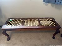 Full view of wooden bench showing three woven rattan sections on top and curved legs.