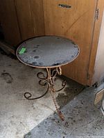 Glass top of the round outdoor bistro table with water spots and dirt marks. Metal base with twisted rope-like design showing rust.