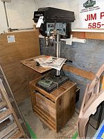 Full front view of drill press on wooden base with instruction manual on table