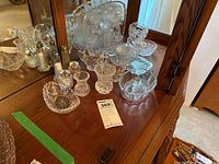 Wide view of glassware including platter, bowls, cream and sugar set, salt and pepper shakers arranged on wooden surface with mirrored background