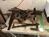 Table surface with multiple vintage hand tools including hand drills, carpenter square, mallet, and saw blades