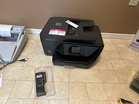 Overall view of black HP OfficeJet Pro 6978 printer and BT-6 battery tester on floor, printer front and top visible.