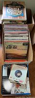 Box of vinyl records including '30 Years of No.1 Country Hits' and 'Ebb Tide' albums, stacked vertically.