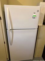 Front-left angled view of white Kenmore refrigerator showing the appliance standing in a garage space, with minor dents visible on the lower door and the door handles in place.