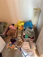 Various sewing and knitting supplies including fabric pieces, plastic storage bins, a rolled carpet or large fabric, and crafting tools arranged on floor.
