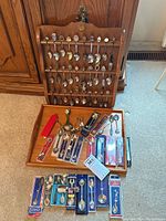 Full view of wooden display stand holding multiple souvenir spoons along with additional spoons grouped below, some in original boxes, showing variety of styles and packaging.