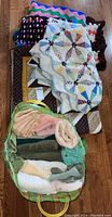 Overview of a basket filled with rolled bath towels in assorted colors alongside layered patchwork quilts and crochet afghans on a wooden floor.