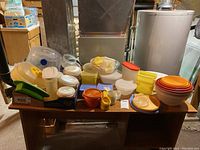Wide view of the table showing various plastic food storage containers and lids of different shapes, sizes, and colors including white, yellow, orange, green, and translucent with some vintage items