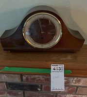 Front view of vintage wooden mantel clock on a wooden surface with clock label 413.